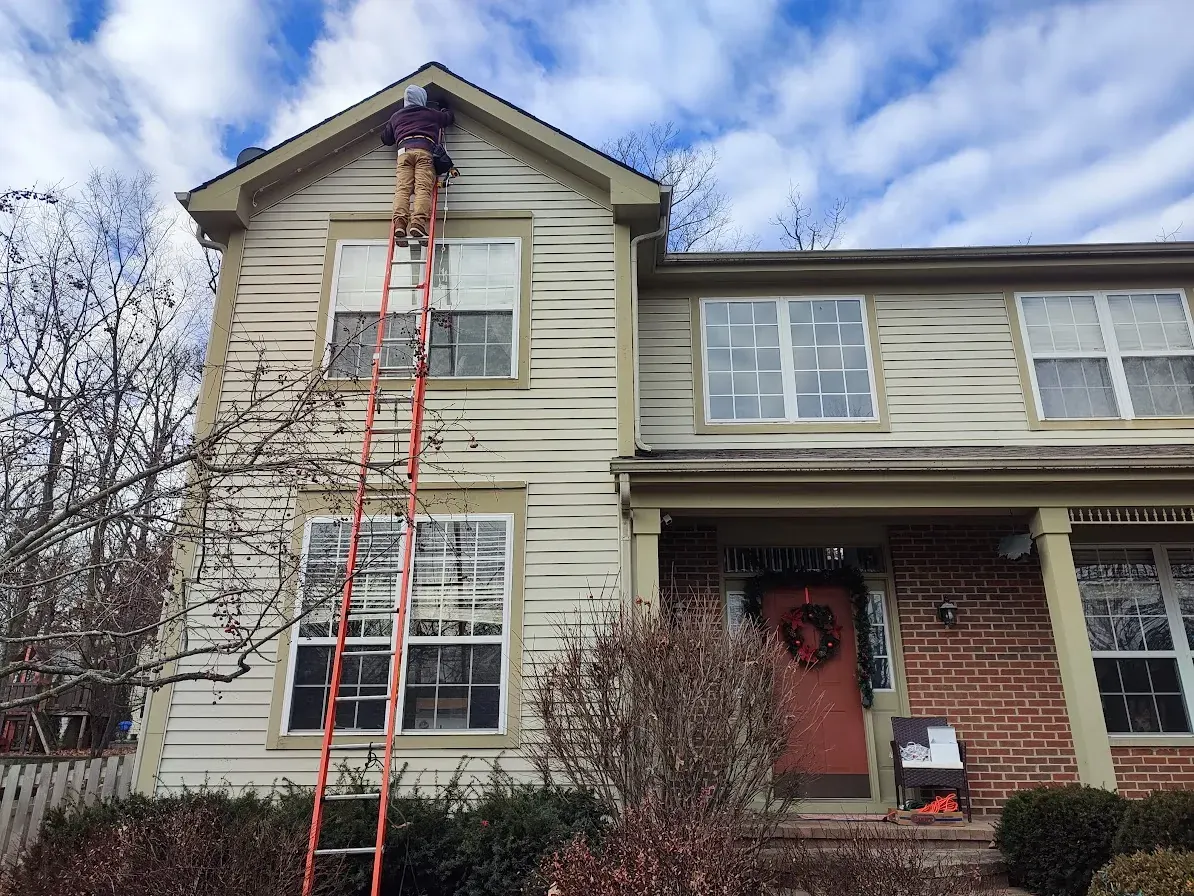 Installer on a tall ladder working at the roof peak of a two-story home