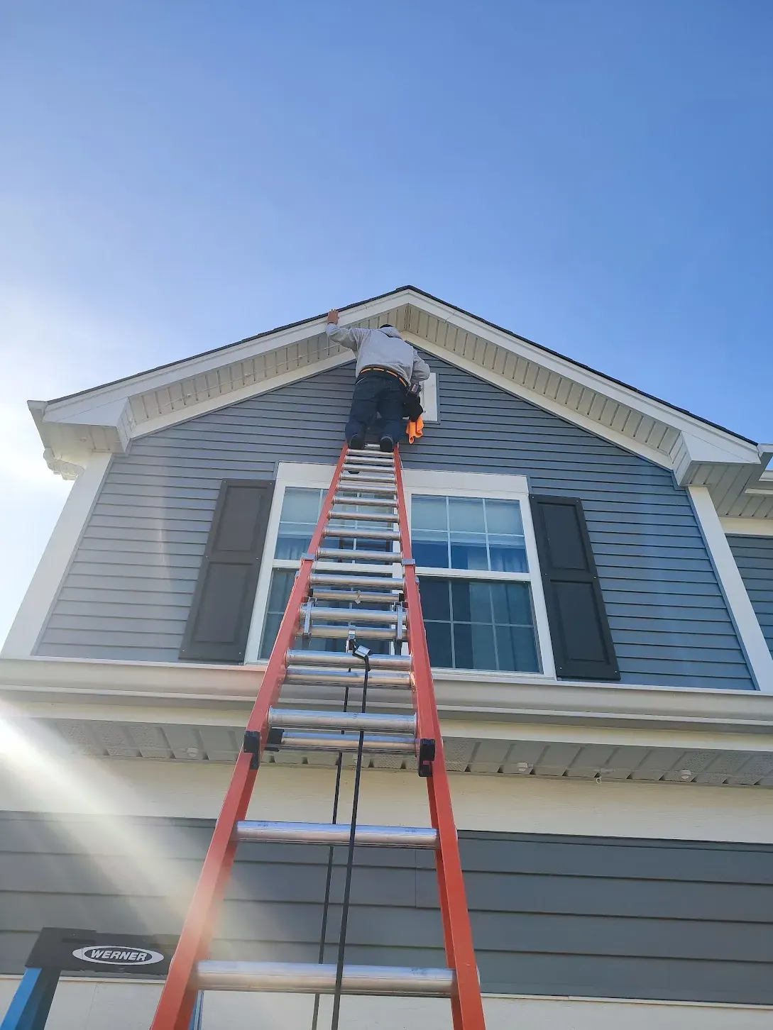 Installer on an extension ladder working at a tall gable peak in daylight